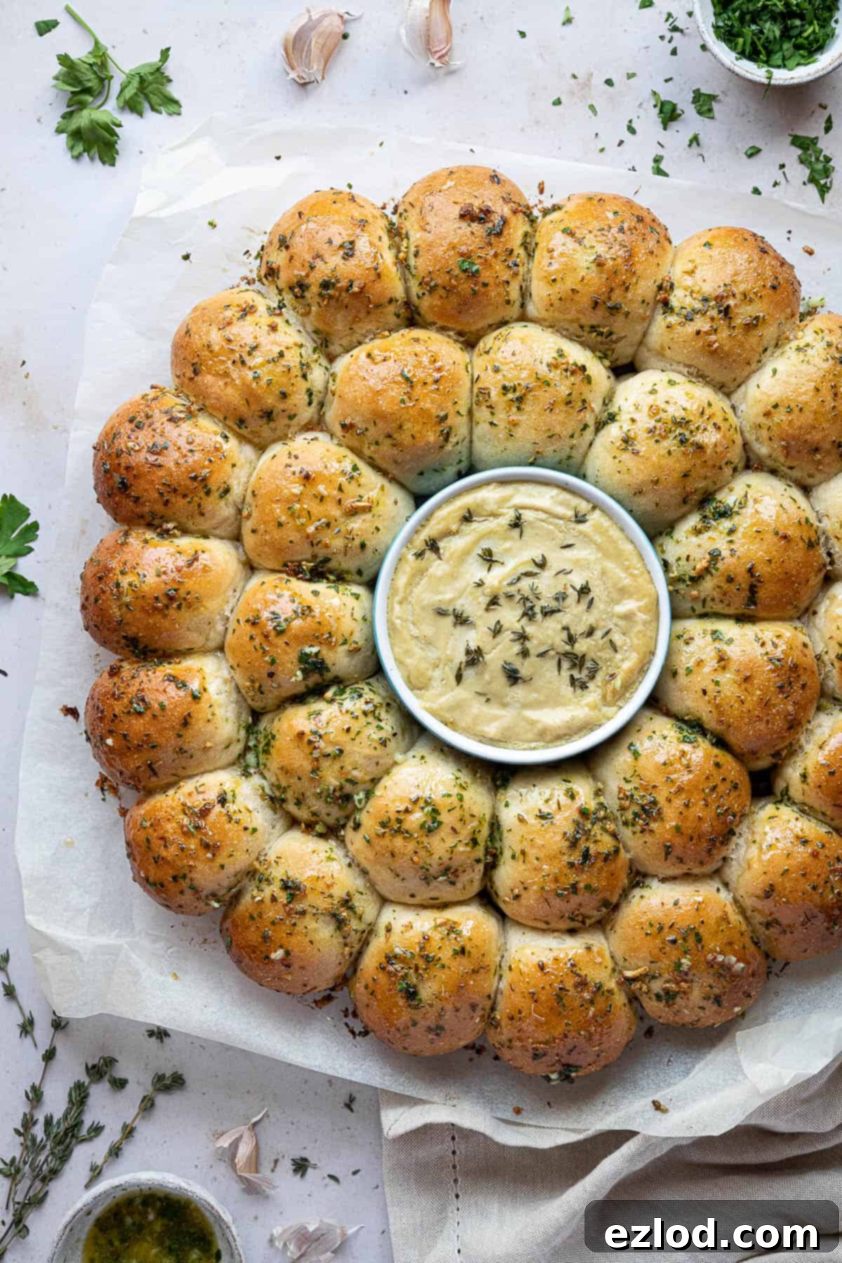 Pillowy Vegan Garlic Dough Balls 13 A top-down view of several warm vegan garlic dough balls arranged around a ramekin of cashew cheese dip, highlighting their inviting texture and golden color.
