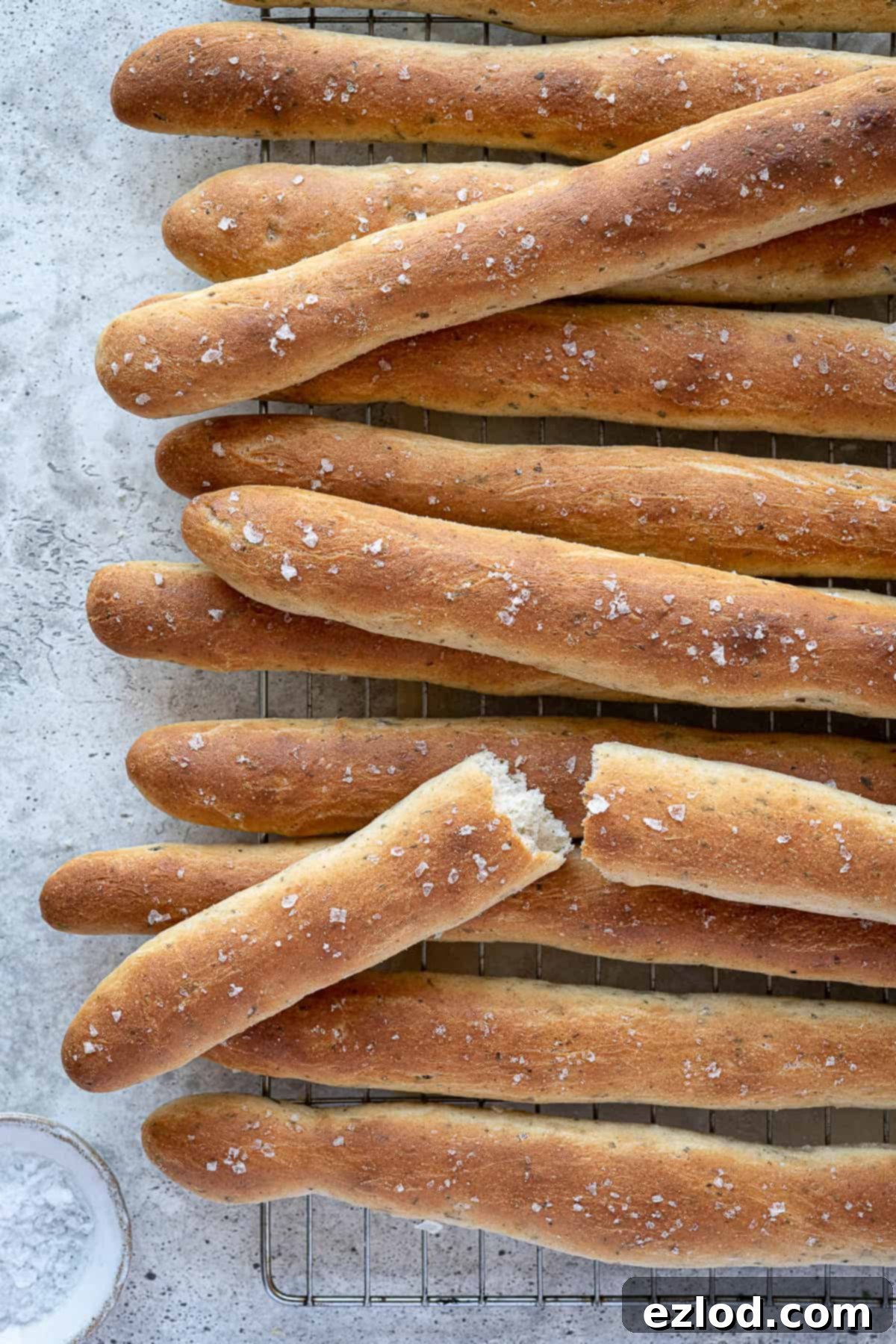 Aromatic Plant Sticks 11 Herby vegan breadsticks cooling on a wire rack, with one broken in half to show its soft interior.