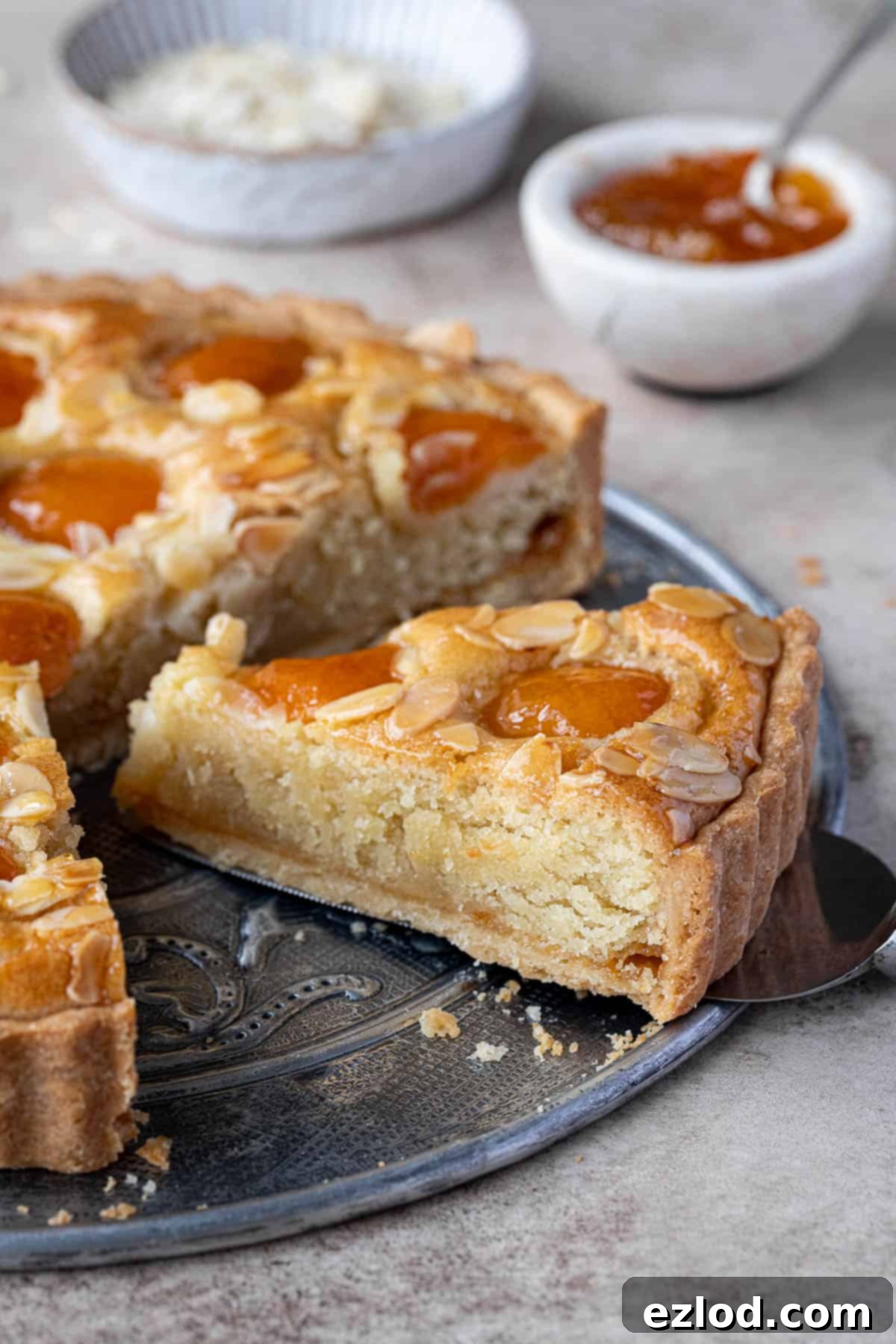 Plant-Based Apricot Frangipane Tart 3 A close-up shot of a single slice of vegan apricot frangipane tart, revealing the layers of crisp pastry, jam, and almond frangipane with apricots on top.