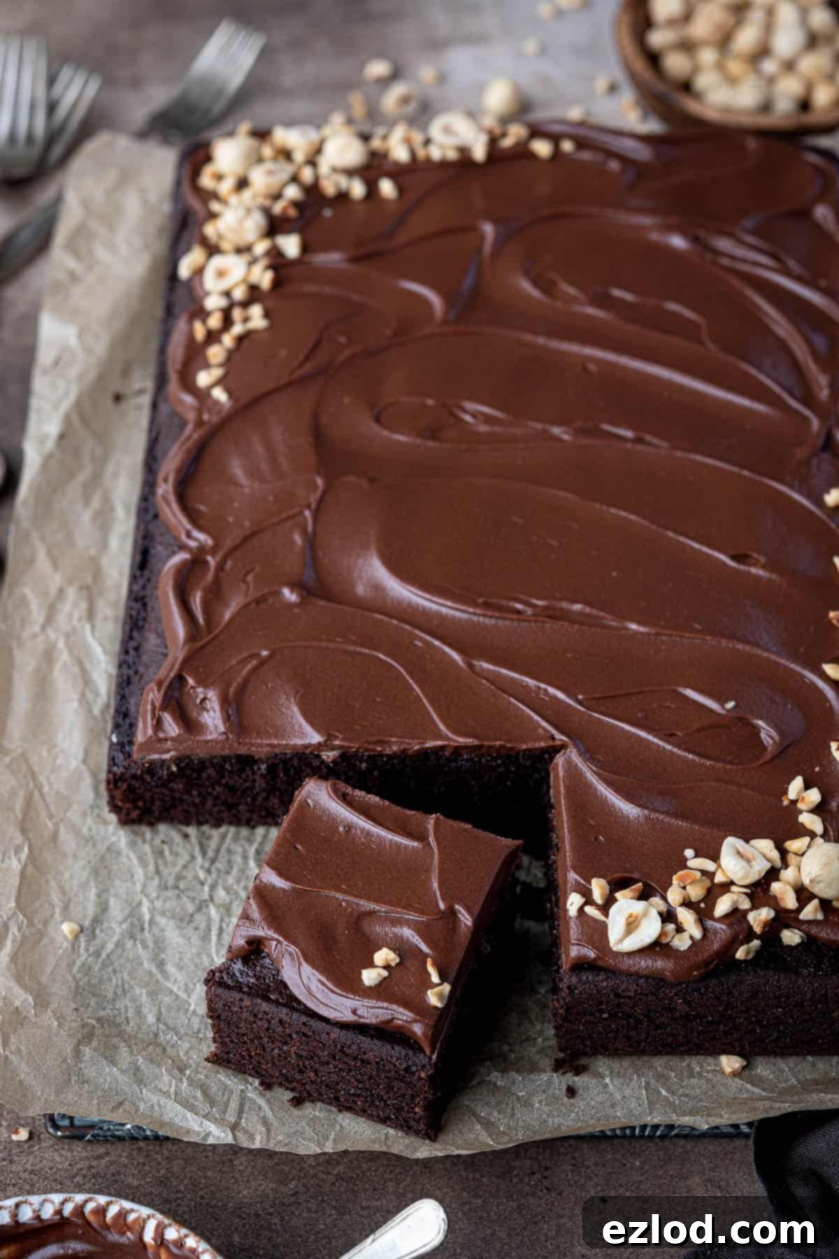 Decadent Vegan Chocolate Hazelnut Cake 12 The fully frosted vegan chocolate hazelnut cake, adorned with chopped roasted hazelnuts, rests beautifully on a sheet of baking parchment, showcasing its indulgent top layer.