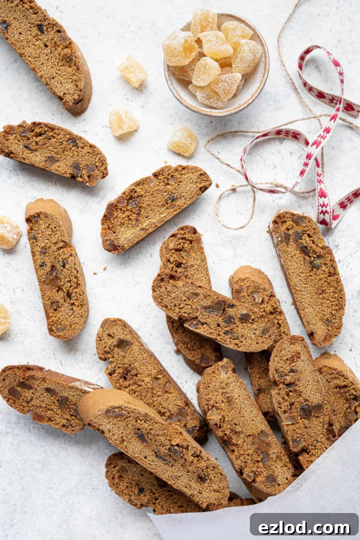 Warmly Spiced Vegan Gingerbread Biscotti 11 Vegan ginger biscotti in a white bag with a bowl of ginger and ribbons.