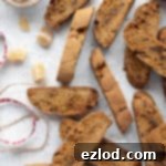 Warmly Spiced Vegan Gingerbread Biscotti 12 Vegan gingerbread biscotti on a white surface with a bowl of candied ginger and some ribbons.