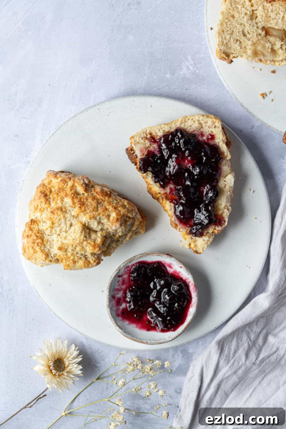 Indulgent Vegan Scones with Marzipan and Glacé Cherries - A Delight for Afternoon Tea! A vegan marzipan cherry scone sliced in half on a white plate, one half generously spread with strawberry jam, showcasing its moist interior.