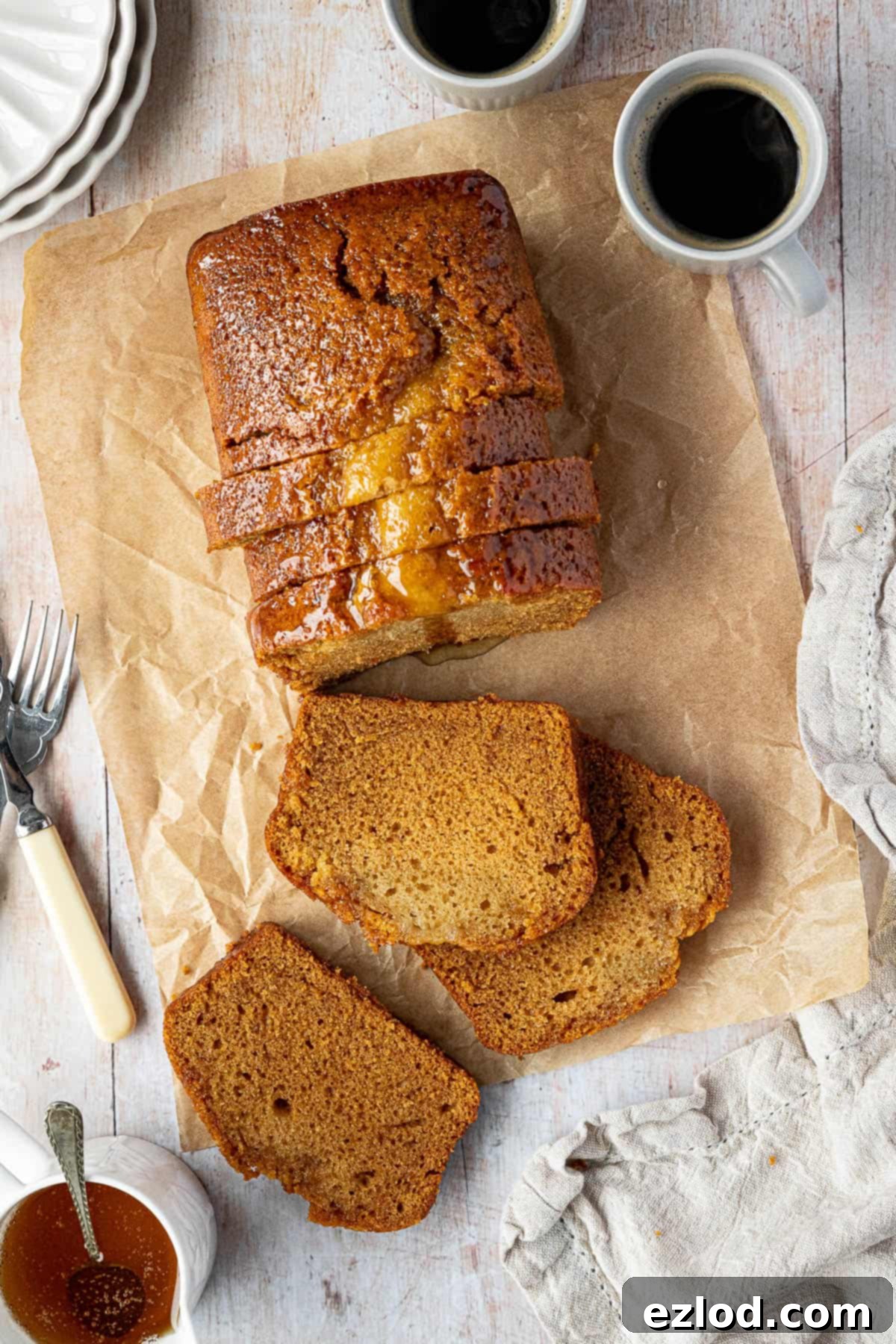 Vegan Liquid Gold Cake 9 The exquisitely sliced vegan golden syrup cake sits invitingly on a wooden table, accompanied by steaming cups of coffee and a charming jug of golden syrup, ready for a cozy gathering.