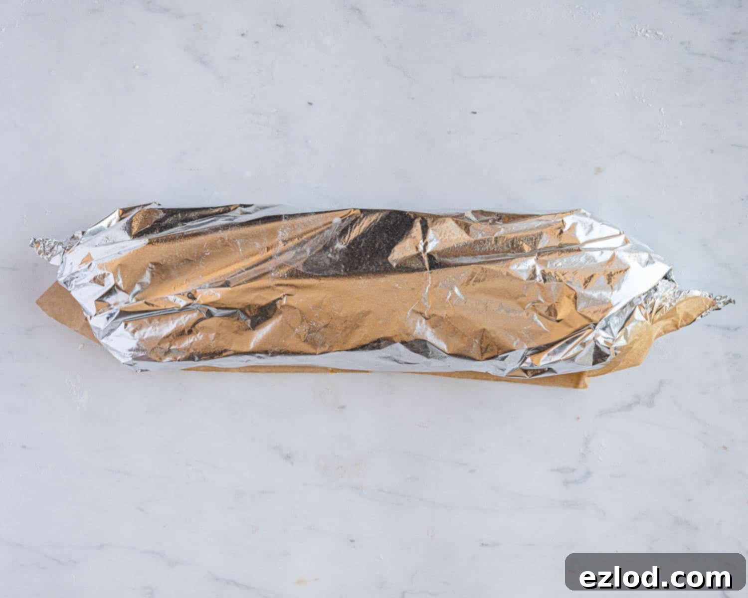 Luscious Vegan Jam Roly-Poly 12 Step 9 in making vegan jam roly-poly: the roly-poly loosely wrapped in baking parchment and tin foil, with the ends twisted to seal the parcel.