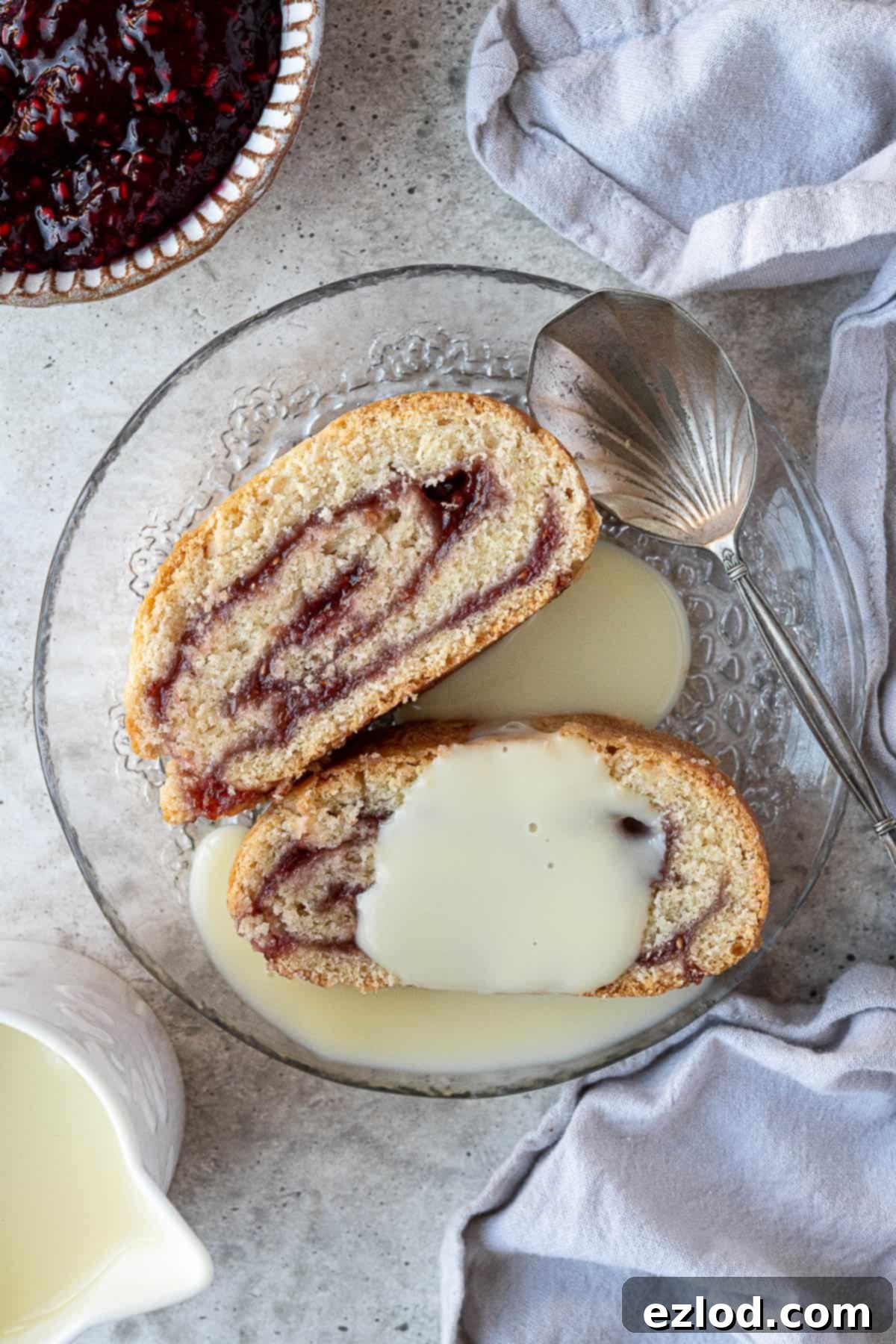 Luscious Vegan Jam Roly-Poly 3 Two generous slices of vegan jam roly-poly on a clear glass plate, served with a pool of creamy vegan custard.
