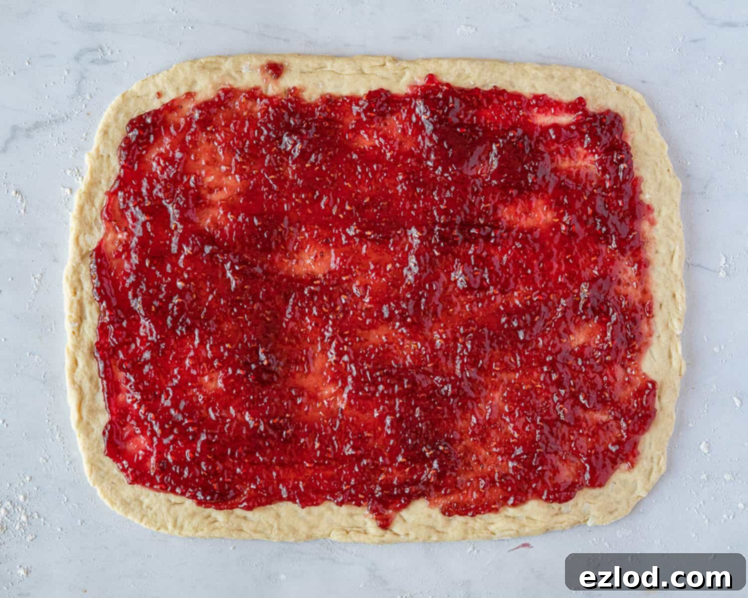 Luscious Vegan Jam Roly-Poly 8 Step 5 in making vegan jam roly-poly: the pastry dough rolled out into a rectangle, generously topped with a layer of red jam, leaving a small border.