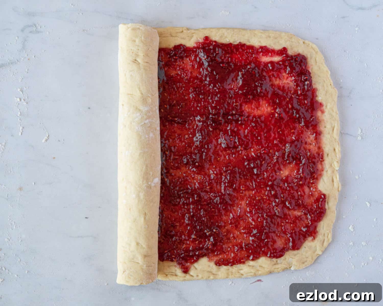 Luscious Vegan Jam Roly-Poly 9 Step 6 in making vegan jam roly-poly: the jam-covered dough being gently rolled up from one short edge to form a log.