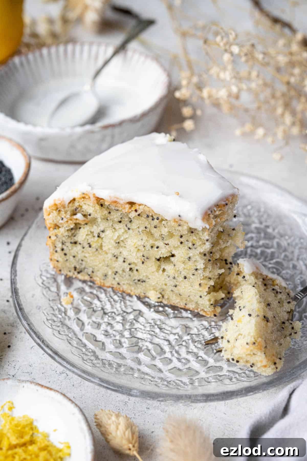 Zesty Vegan Lemon Poppy Seed Cake 2 A beautifully presented slice of vegan lemon poppy seed cake on a glass plate with a forkful gently removed, highlighting its moist crumb and delicate poppy seeds.