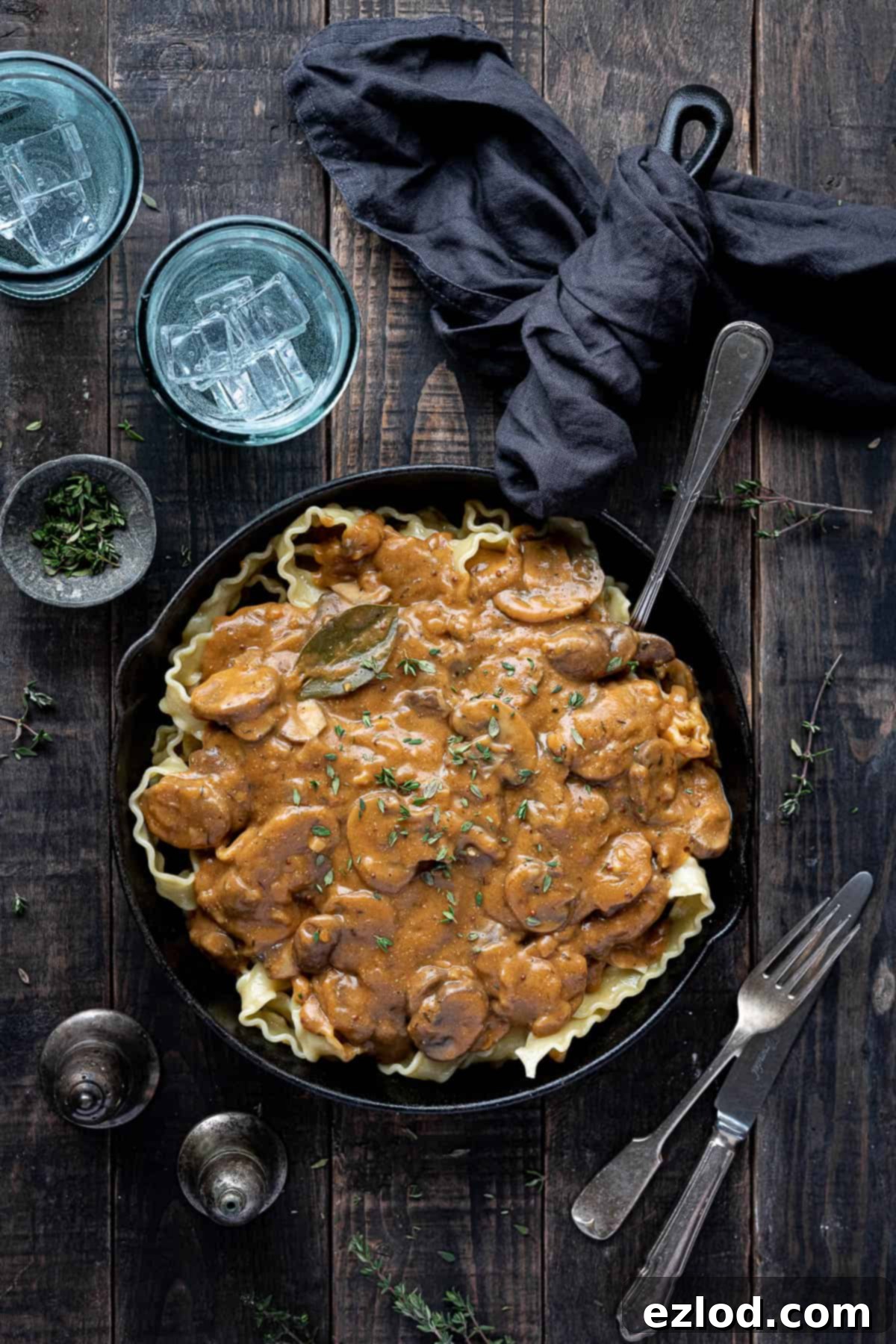 Creamy Vegan Mushroom Stroganoff 2 Vegan mushroom stroganoff on top of pasta in a skillet with glasses of water and fresh thyme.