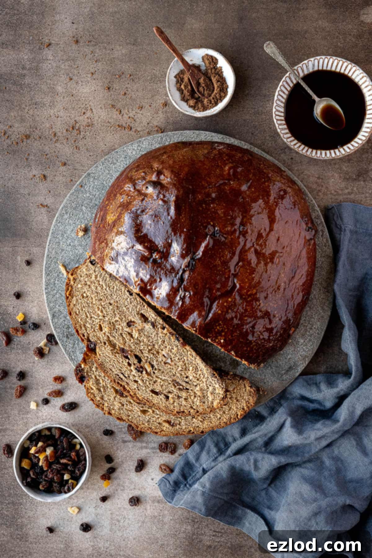 Jamaican Plant-Based Spiced Bun 3 A whole Jamaican spice bun displayed on a rustic stone plate, with small bowls of glaze, dried fruit, and spices in the background.
