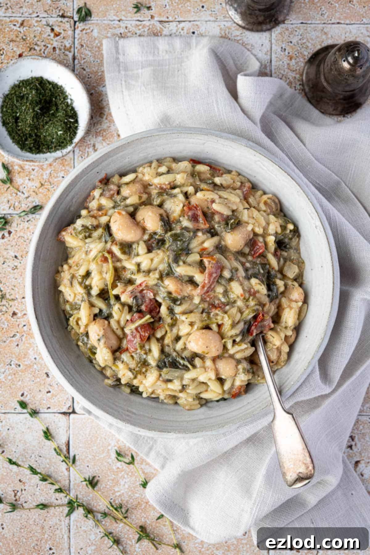 Velvety Vegan Spinach Orzo 9 A white bowl of creamy spoinach orzo pasta with a napkin, salt and pepper shakers and a bowl of dried herbs.