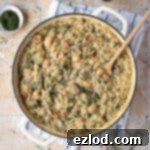 Velvety Vegan Spinach Orzo 10 A pan of creamy spinach orzo on a tiled surface with salat and pepper shakers, forks and a bowl of dried herbs.