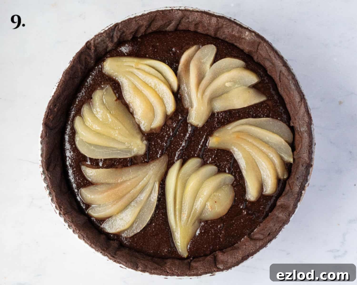 Rich Vegan Chocolate Pear Almond Tart 13 Step-by-step image showing fanned poached pears artfully arranged over the chocolate frangipane filling in the tart shell, before baking.