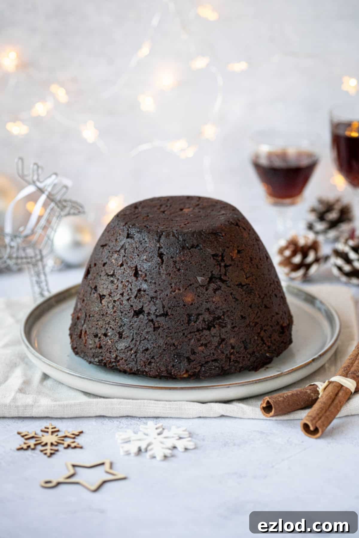 Guilt-Free Vegan Chocolate Christmas Pudding 2 Vegan chocolate Christmas pudding on a plate surrounded by Christmas decorations and glasses of rum.