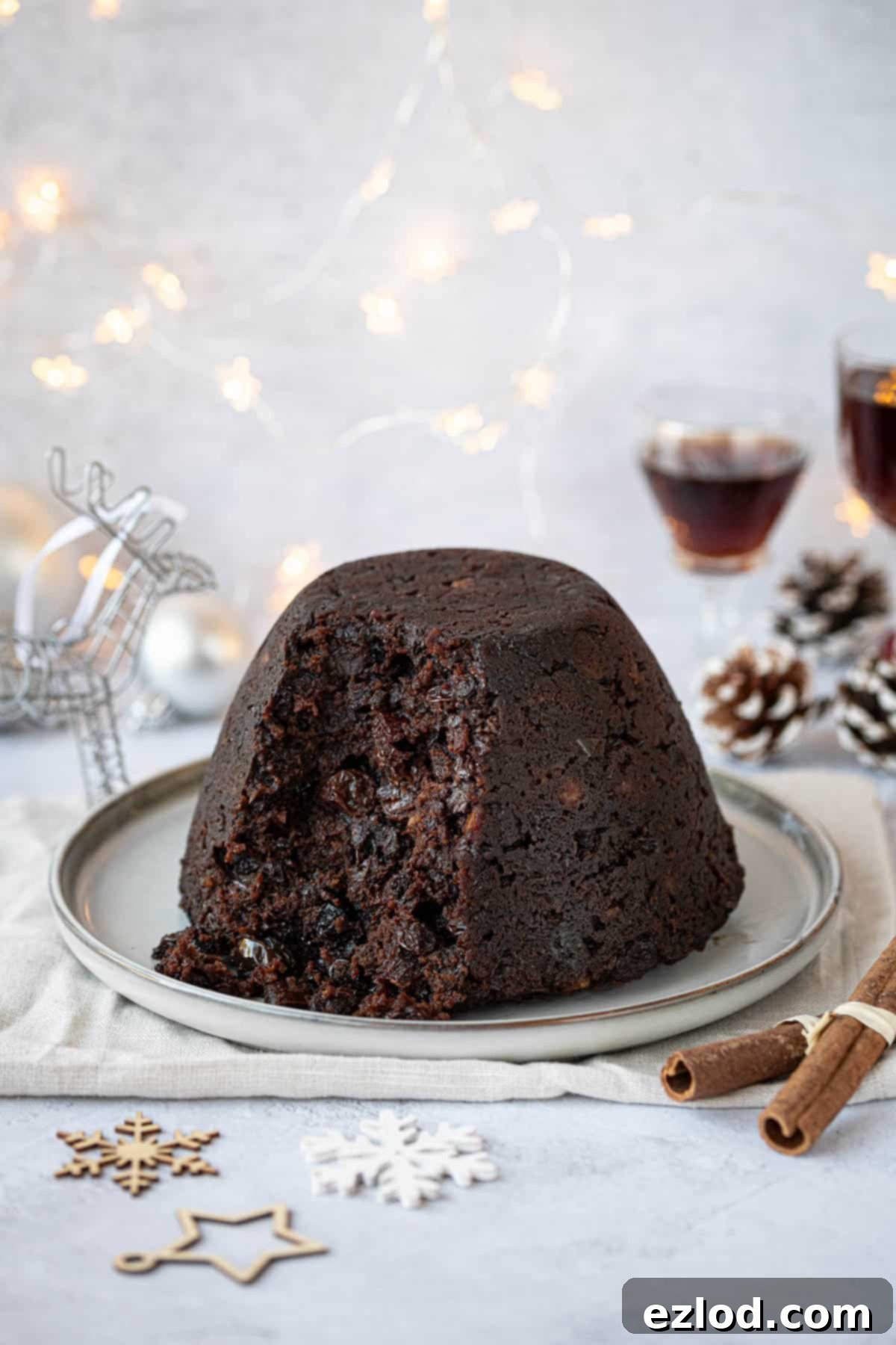 Guilt-Free Vegan Chocolate Christmas Pudding 13 Vegan chocolate Christmas pudding with a spoonful removed, surrounded by festive decorations, fairy lights and glasses of rum.