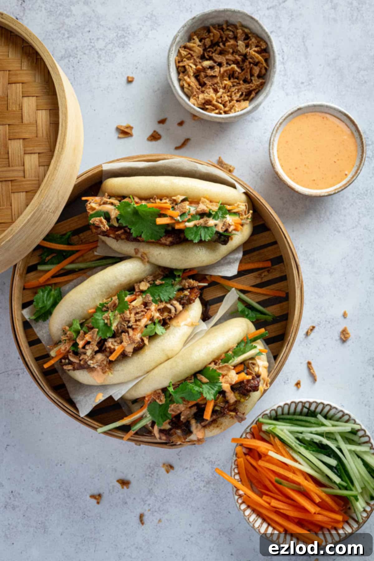 Pillowy Vegan Hoisin Tofu Bao Buns 9 Three hoisin tofu bao buns artfully arranged in a bamboo steamer, surrounded by bowls of fresh ingredients.