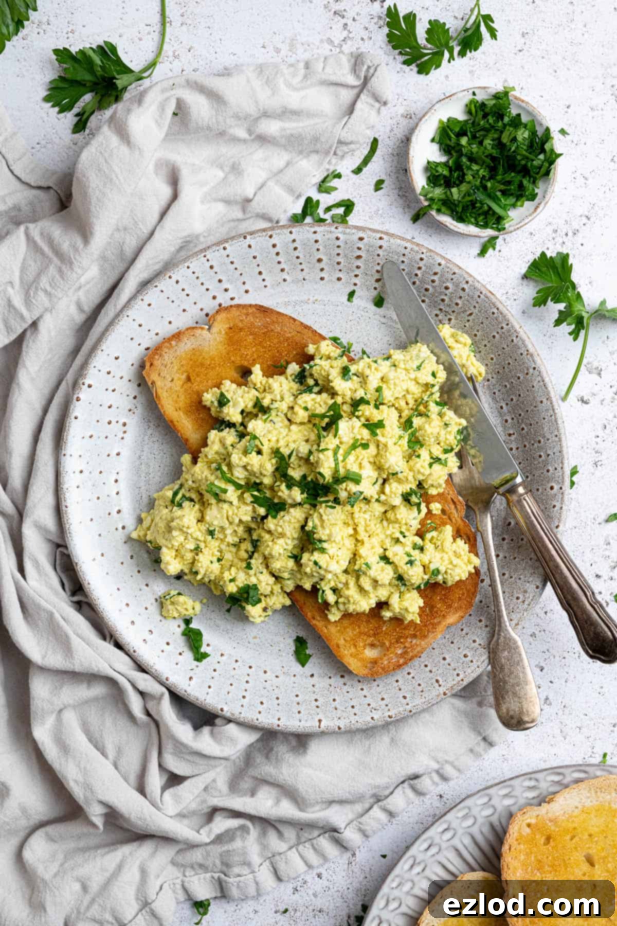 Golden Tofu Scramble 3 Close-up of fluffy tofu scramble delicately placed on a slice of golden toast, served on a white plate.