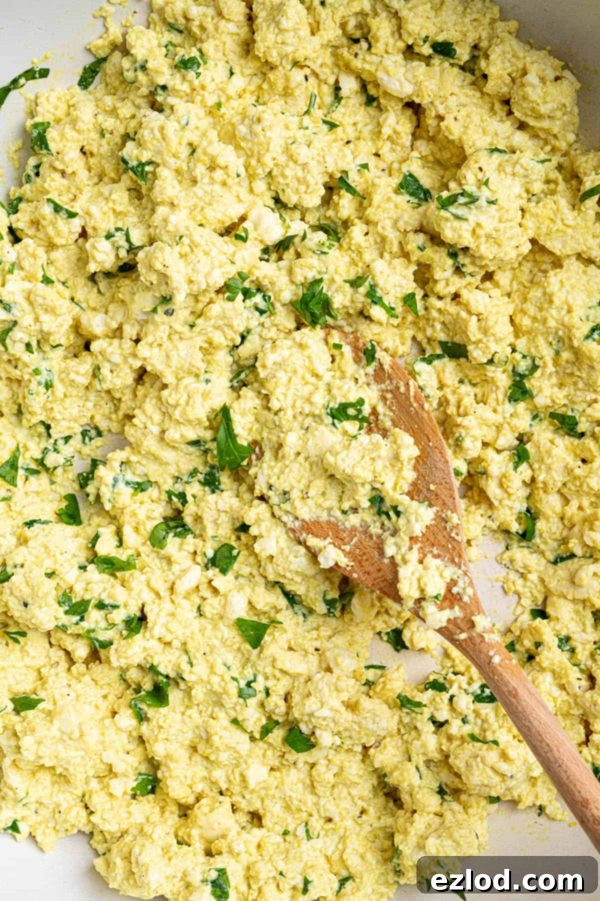 Golden Tofu Scramble 5 A close-up view of the perfectly cooked tofu scramble, rich with seasonings, being stirred in a pan with a wooden spoon.