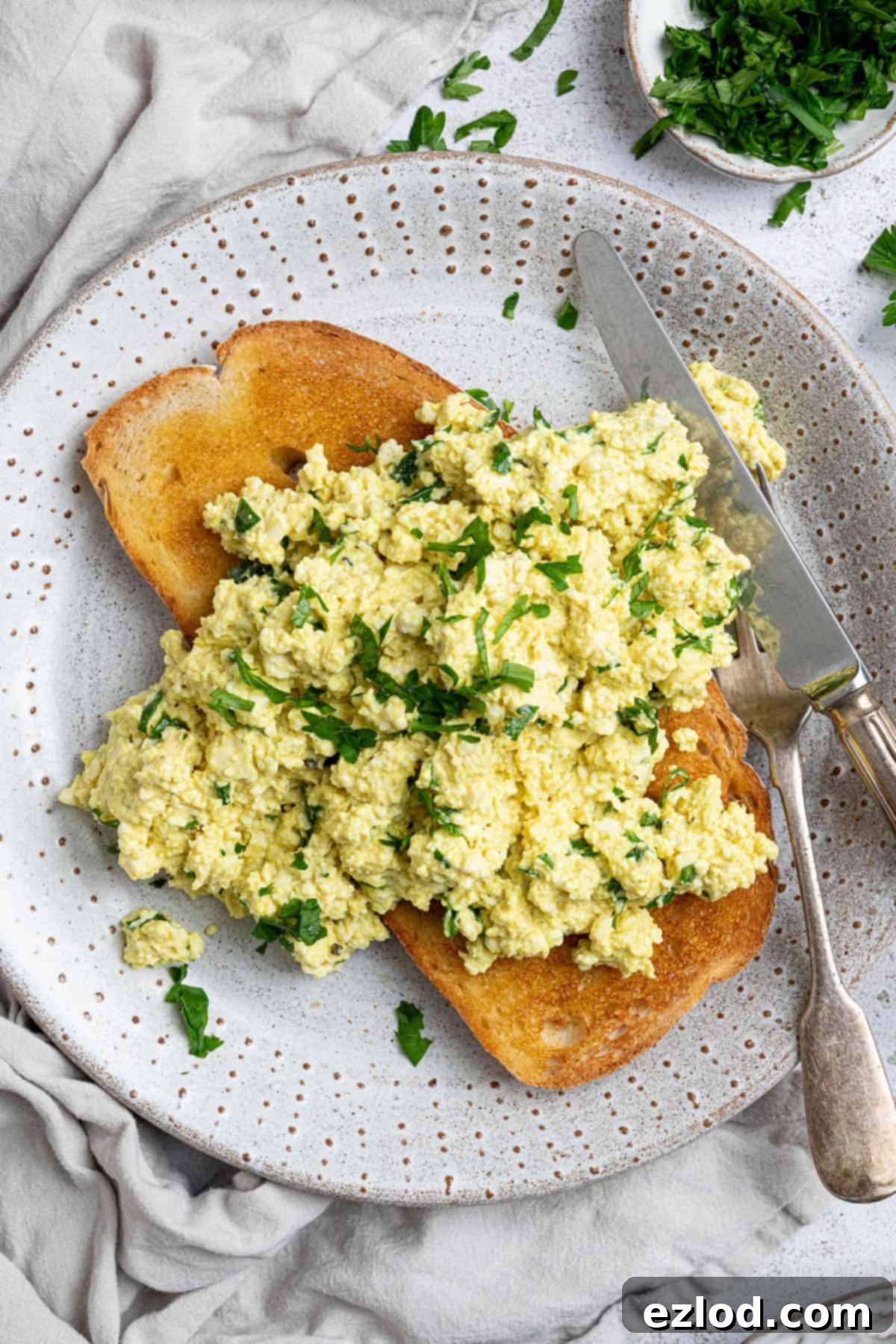 Golden Tofu Scramble 6 Close-up of fluffy tofu scramble on a piece of golden toast, garnishing with fresh parsley, ready to eat.