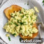 Golden Tofu Scramble 7 Close-up of fluffy tofu scramble on a piece of golden toast, garnishing with fresh parsley, ready to eat.