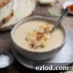Velvety Vegan Roasted Garlic Cauliflower Soup 13 A bowl of roasted garlic cauliflower soup on a plate with a sliced loaf of bread.
