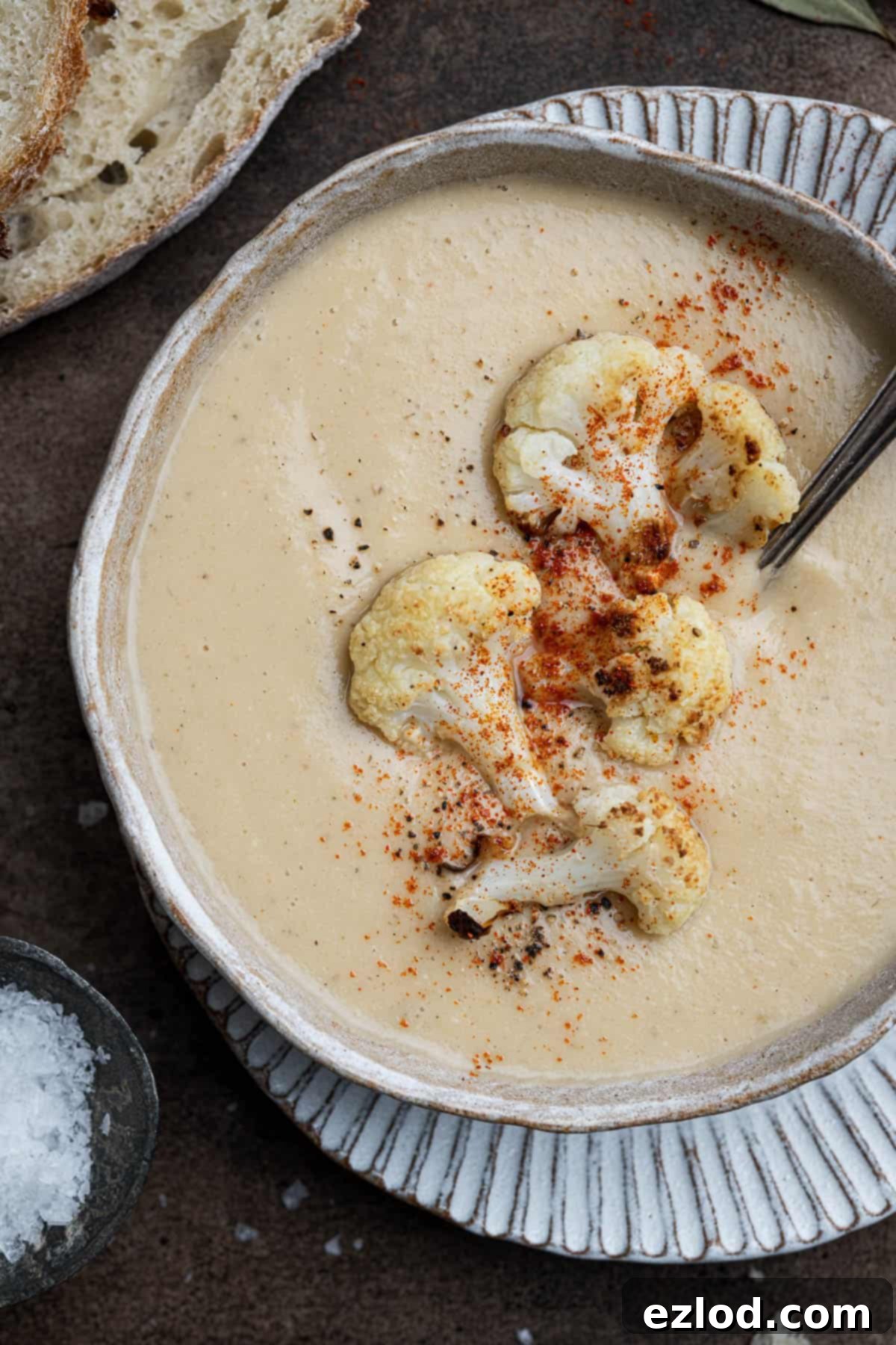 Velvety Vegan Roasted Garlic Cauliflower Soup 4 A close-up shot of a bowl of rich roasted garlic cauliflower soup, garnished with delicate roasted cauliflower florets and fresh herbs.