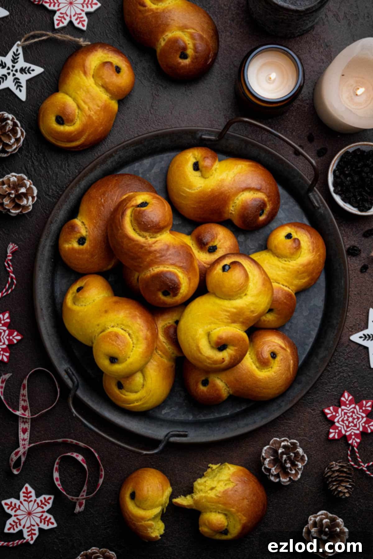 Plant-Based Saffron Buns for St. Lucia 16 Vegan lussekatter on a round metal serving tray surrounded by candles and ornaments.