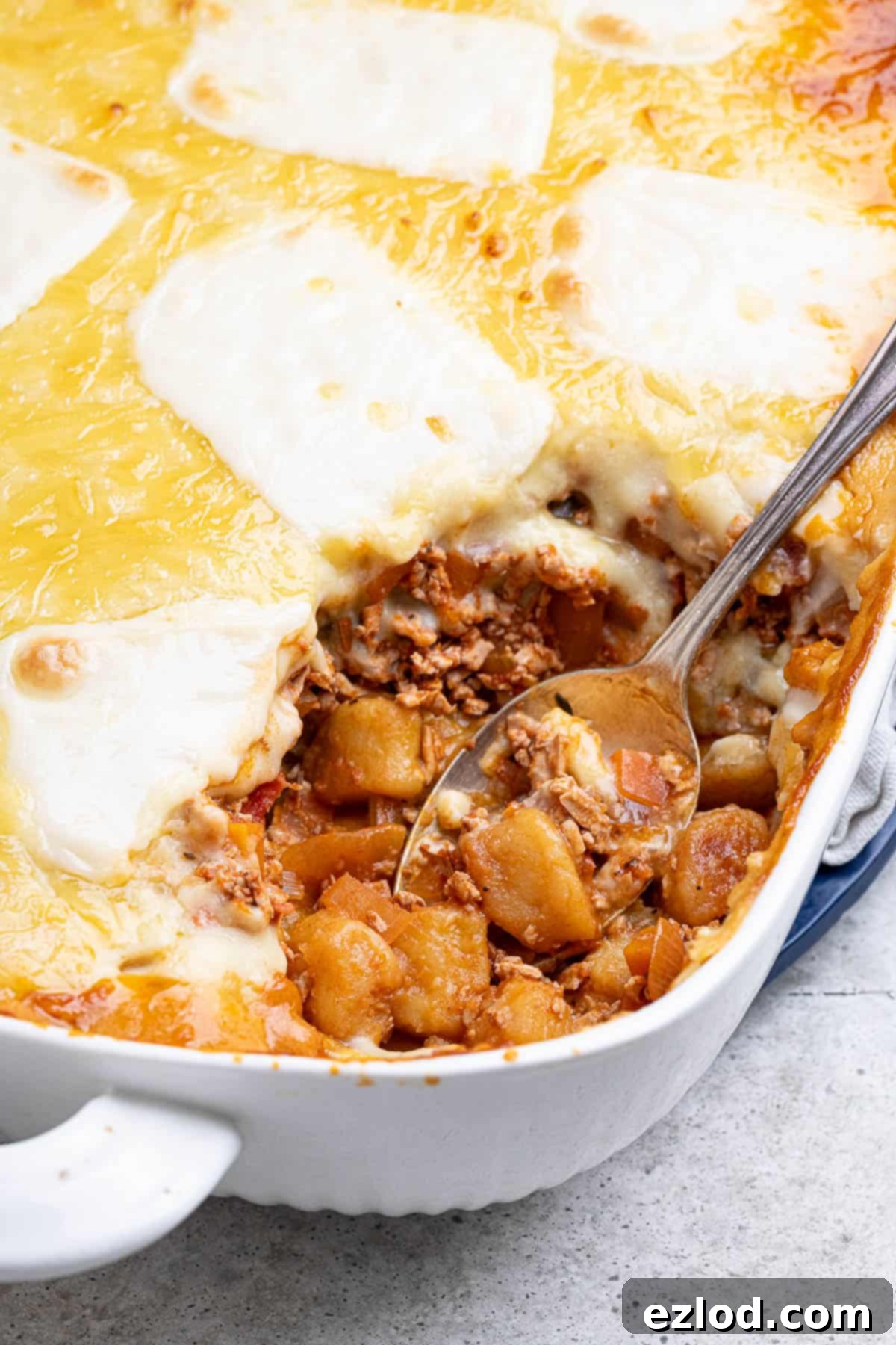 Gooey Vegan Gnocchi Bake 11 Close-up of the cheesy vegan gnocchi bake in a white dish, with a serving spoon scooping out a generous portion, highlighting the rich layers.