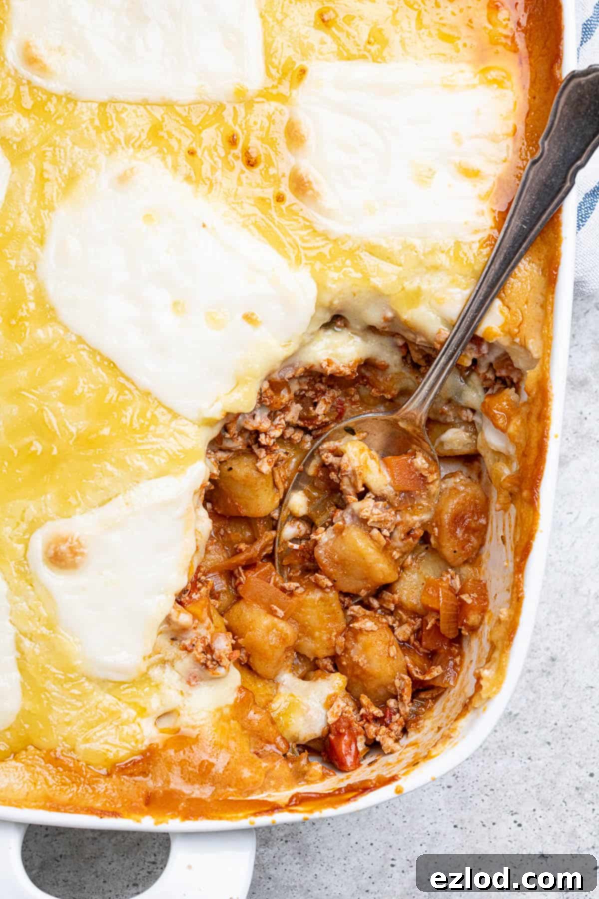 Gooey Vegan Gnocchi Bake 4 A close-up view of the perfectly baked cheesy vegan gnocchi bake, showing its golden-brown top, bubbling cheese, and rich, layered interior in a white baking dish.