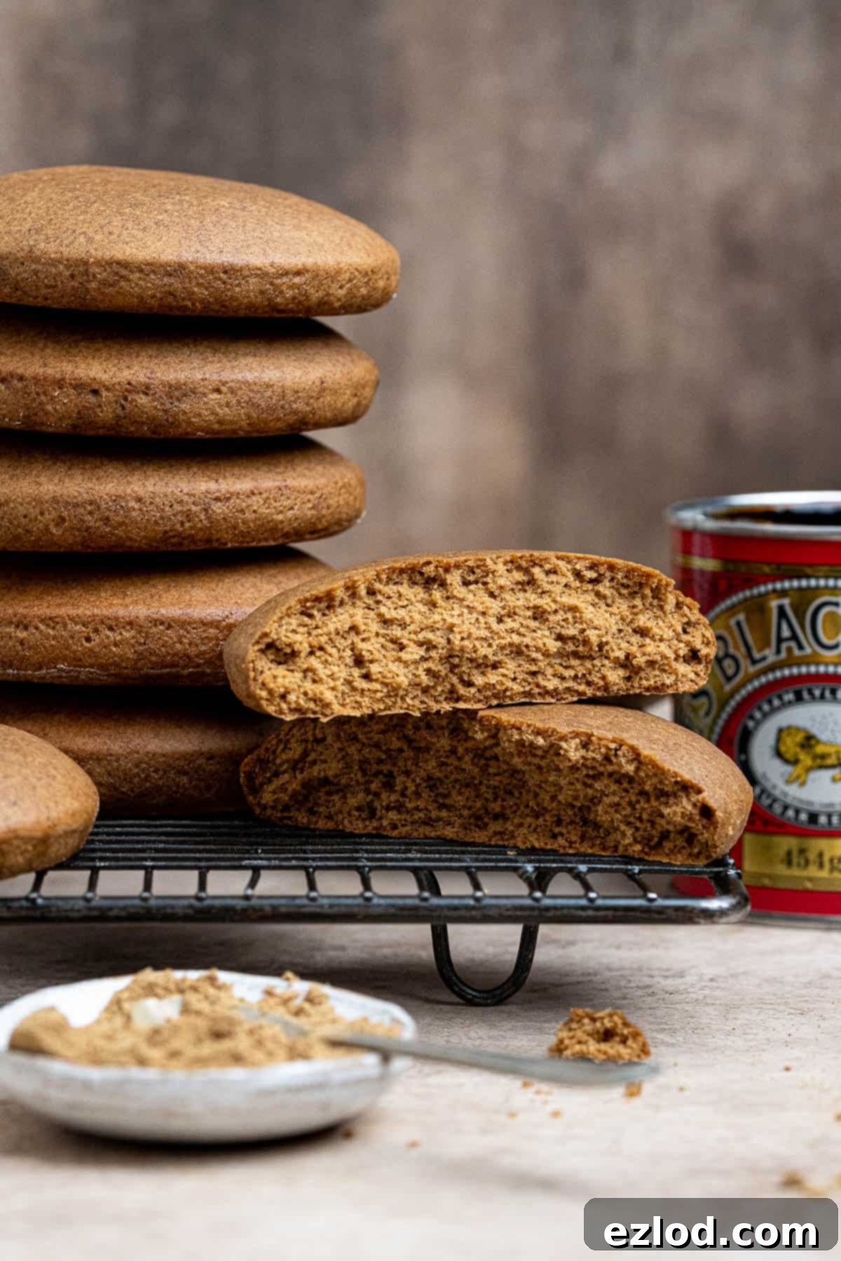 Plant-Based Jamaican Bulla Delight 2 Stacks of warm, golden-brown vegan Jamaican ginger bulla cakes on a wire cooling rack, with fresh ginger and a tin of molasses in the soft-focus background, highlighting key ingredients.