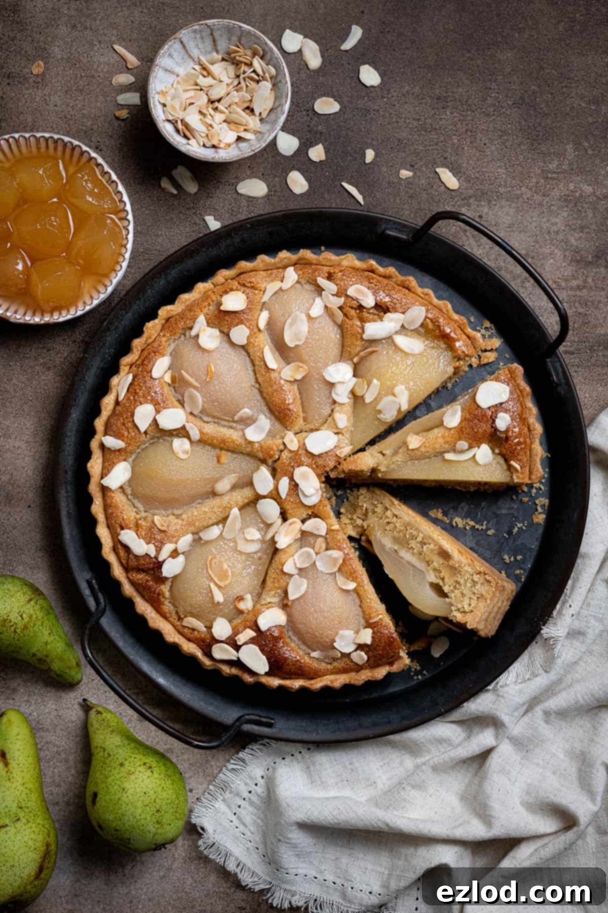 Gingered Pear & Almond Vegan Tart 15 The elegantly sliced vegan pear, ginger, and almond tart displayed on a metal tray, with accompanying bowls of stem ginger and flaked almonds, alongside fresh pears.