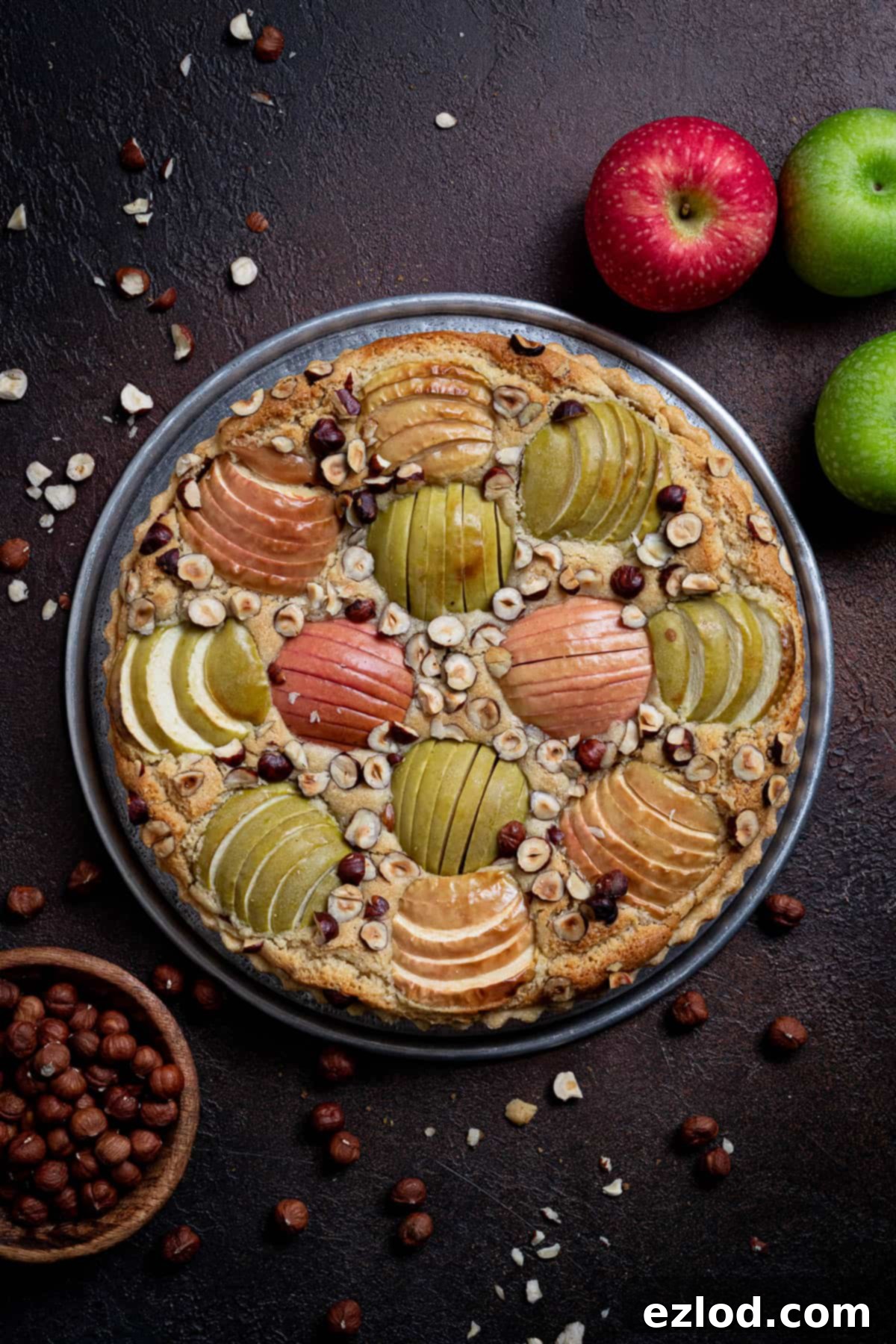 Elegant Vegan Apple Hazelnut Frangipane Tart 2 A stunning vegan apple hazelnut frangipane tart on a dark rustic background, adorned with fresh apples and a bowl of roasted hazelnuts, perfect for autumn baking.