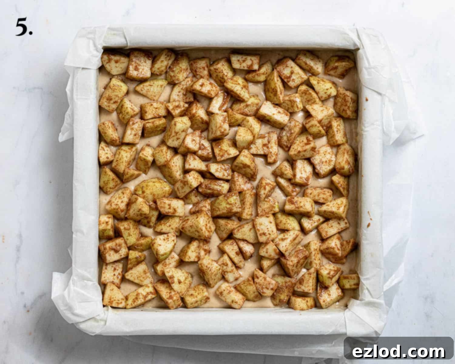 Spiced Vegan Apple Streusel Cake 9 Step 5, the first layer of cake batter in the lined tin, topped with an even layer of seasoned apples.