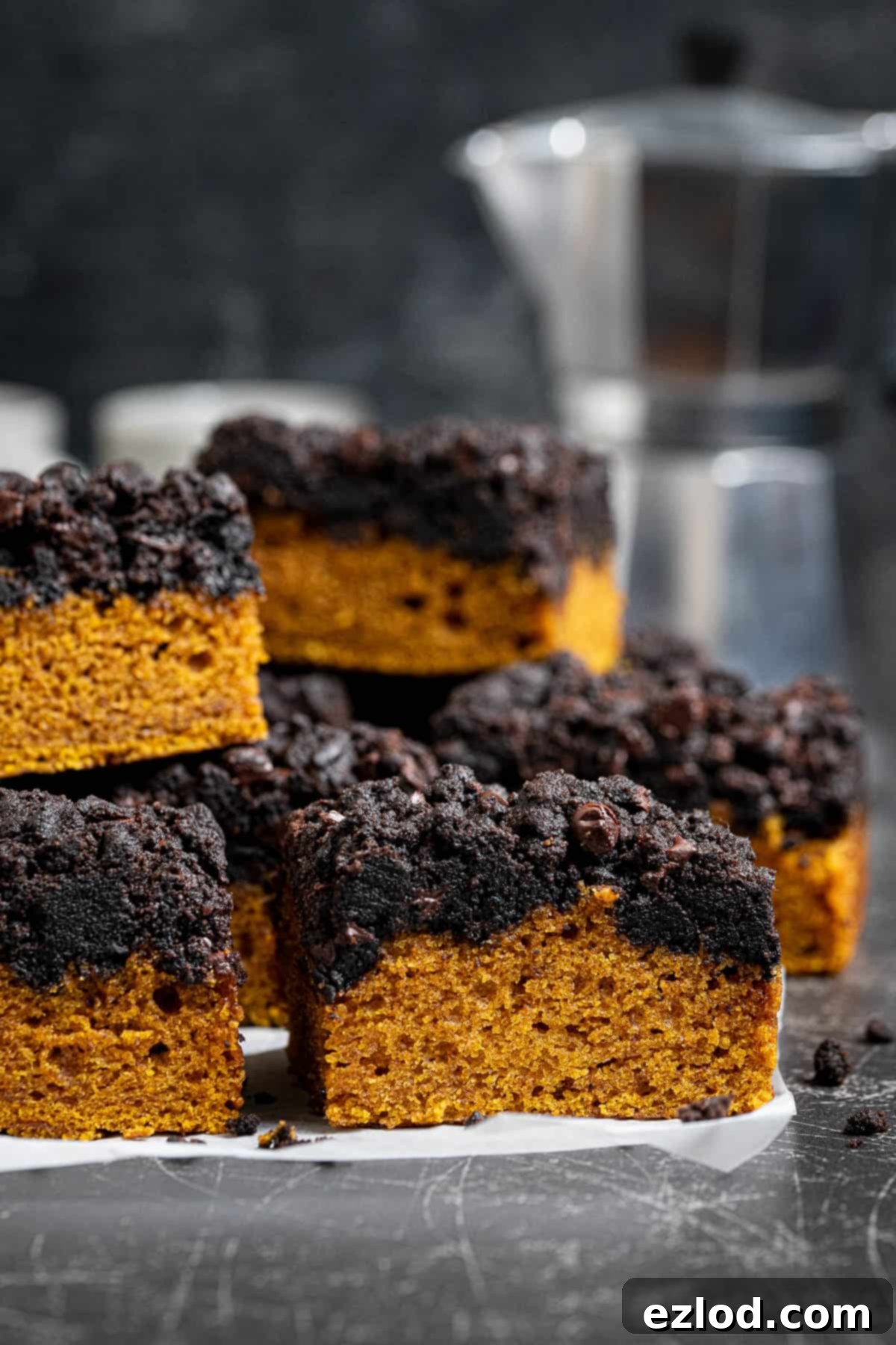 A stack of squares of vegan pumpkin crumb cake with a coffee pot.