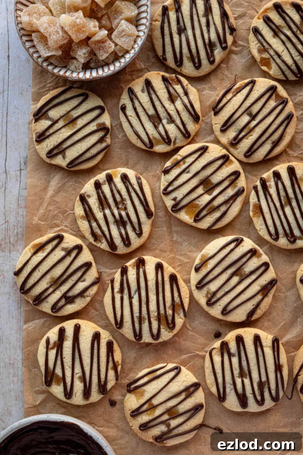 Buttery Ginger Shortbread 13 Ginger shortbread cookies on a sheet of brown baking parchment with bowls of candied ginger and chocolate.
