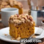 Spiced Vegan Pumpkin Streusel 12 A square of vegan pumpkin crumb cake on a white plate with a fork and a pot of coffee in the background.