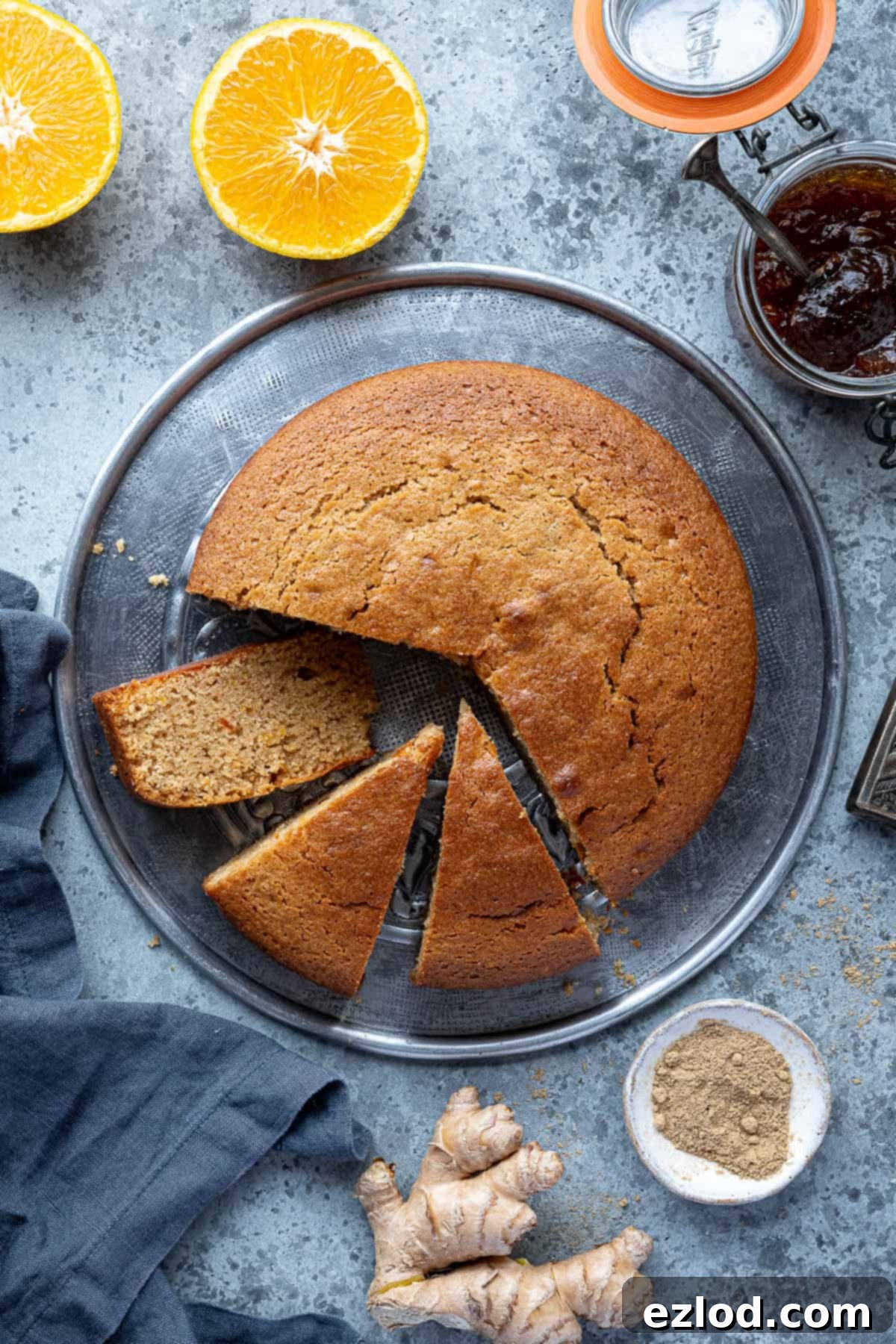 Sun-Kissed Vegan Ginger Cake with Tangy Marmalade 3 A whole vegan marmalade and ginger cake presented on a metal plate, artfully surrounded by fresh orange slices, a jar of marmalade, and both fresh and dried ginger for a vibrant display.