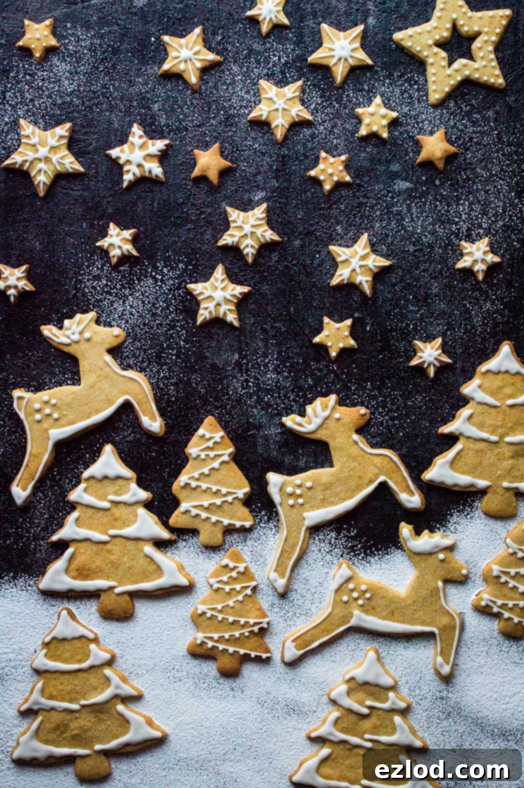 Beautifully arranged orange cinnamon butter biscuits in various festive shapes like stars, snowflakes, reindeers, and Christmas trees, decorated with white royal icing, creating an inviting holiday scene.