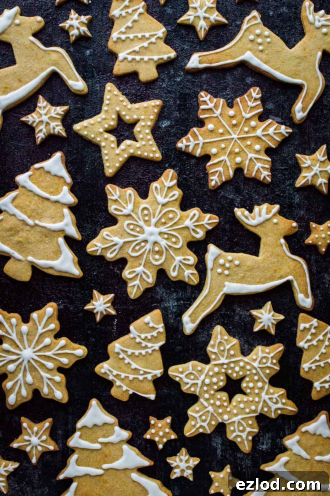 Top-down view of a delightful assortment of orange cinnamon butter biscuits, shaped as reindeer, Christmas trees, stars, and snowflakes, ready for baking or cooling on a parchment-lined tray.