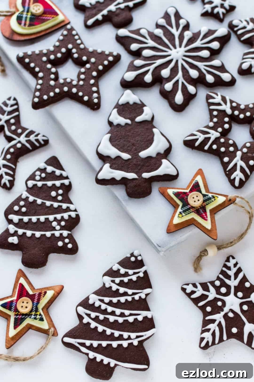 Vegan Chocolate Gingerbread Cookies 4 Angled photo of iced chocolate gingerbread biscuits on a white marble board with wooden Christmas tree decorations.