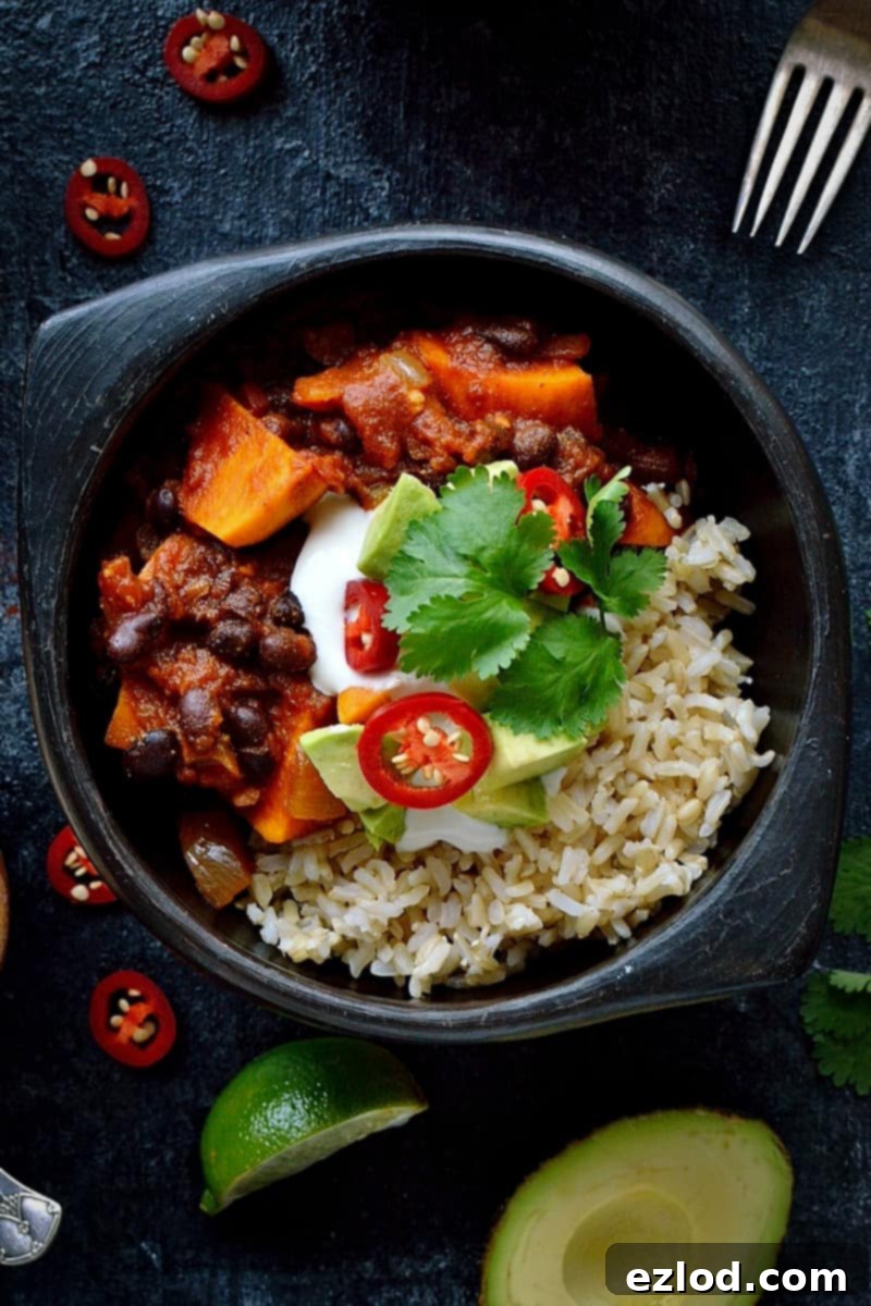 Hearty Vegan Sweet Potato Black Bean Chili 5 Sweet potato black bean chilli, generously topped with an array of garnishes including sour cream, cheese, avocado, and fresh cilantro, served alongside brown rice. This image emphasizes the hearty, filling, and delicious nature of this vegan meal.