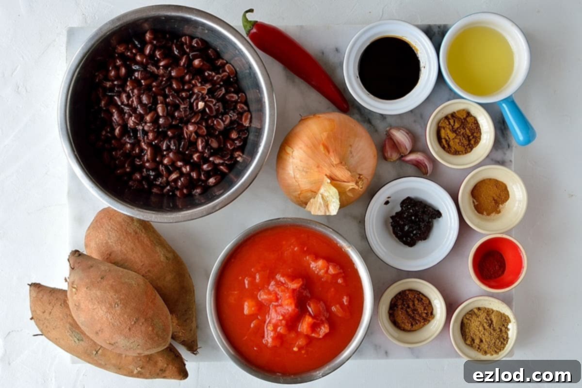 Hearty Vegan Sweet Potato Black Bean Chili 6 Ingredients for sweet potato black bean chilli laid out on a counter, including sweet potatoes, black beans, tomatoes, onions, garlic, and various spices, ready for cooking.