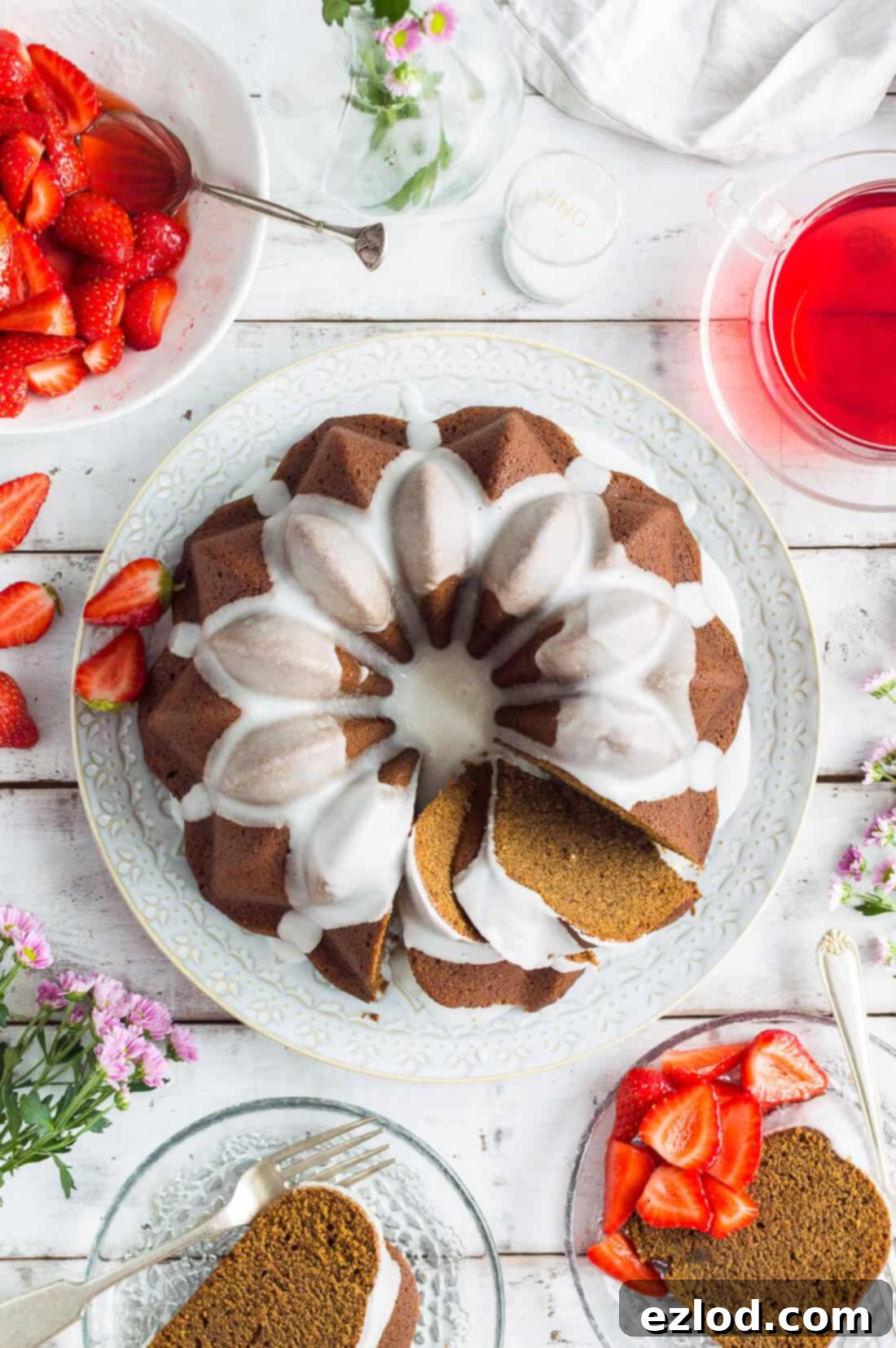 Vegan Ginger Bundt with Zesty Lime Drizzle and Sweet Strawberries 7 A top down shot of sliced vegan ginger bundt cake with lime glaze, macerated strawberries and green apple and hibiscus herbal tea on a white wooden background.