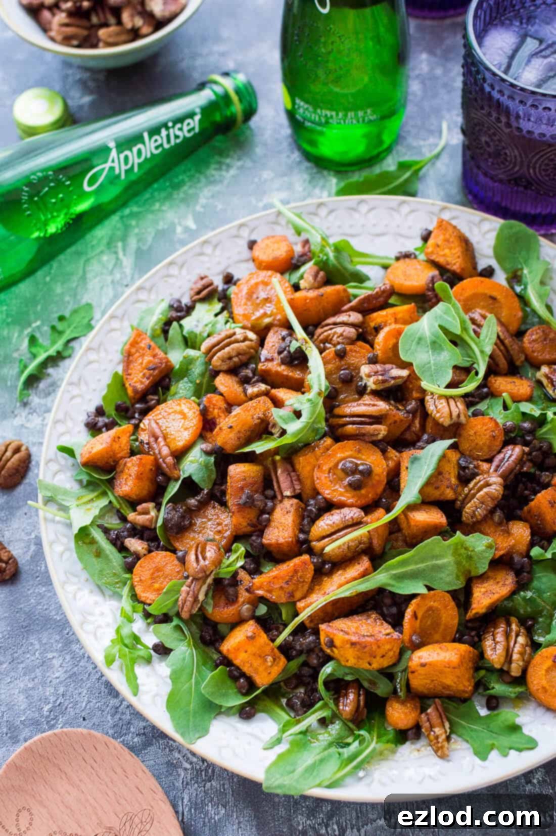 Wholesome Roasted Sweet Potato and Lentil Arugula Bowl 4 Roasted sweet potato, lentil and rocket salad with toasted pecans on a white plate with Appletiser on a grey background.