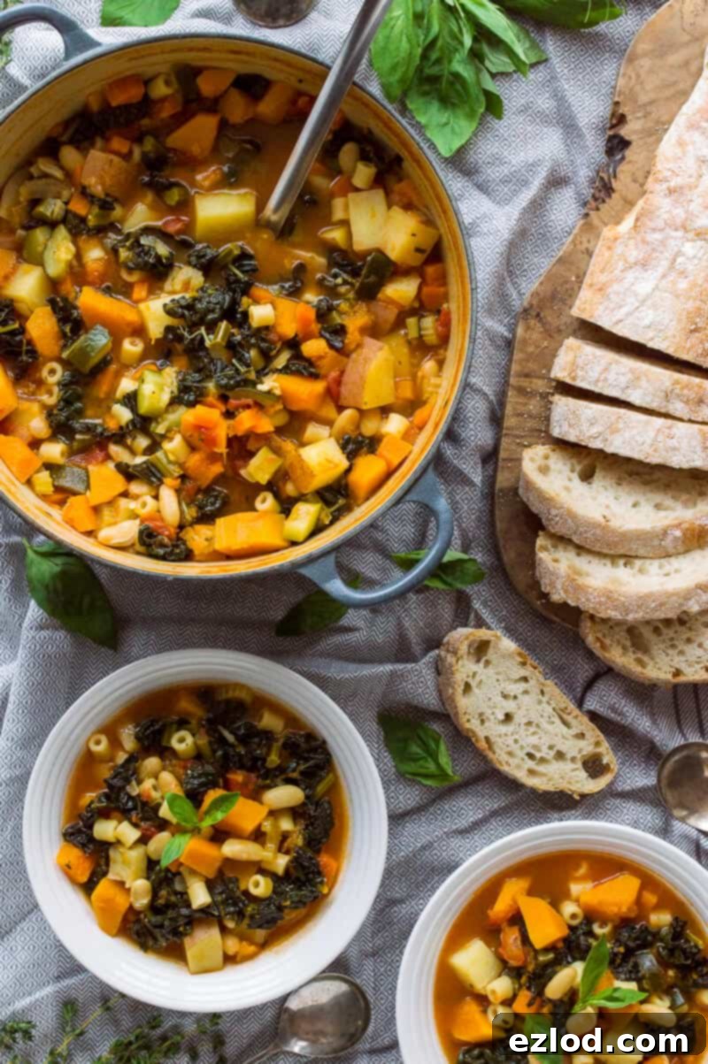 Cozy Vegan Fall Minestrone 4 A large pot of vibrant vegan autumn minestrone soup on a stovetop, with two individual bowls and sliced ciabatta on a nearby grey tablecloth, illustrating a complete meal setting.