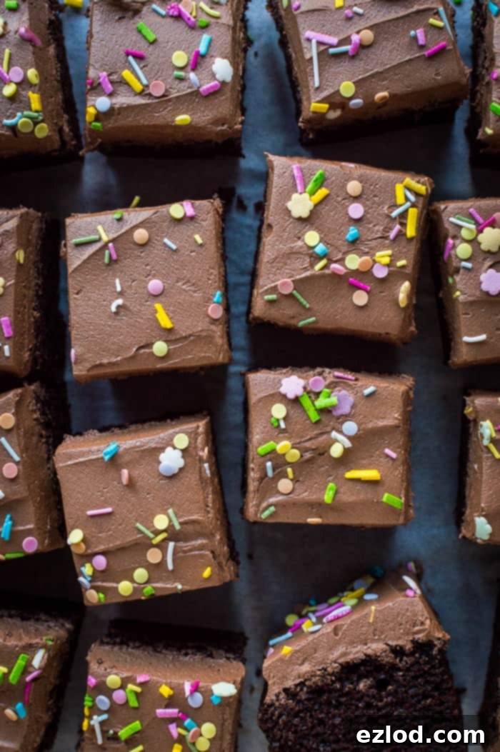 Easy vegan chocolate cake - this simple vegan chocolate sheet cake is quick and easy to make and doesn't use any unusual or hard to find ingredients. It is so moist and rich you would never guess that it is free from eggs and dairy! A close-up view of individual squares of this easy vegan chocolate cake, generously topped with smooth vegan chocolate buttercream and festive sprinkles, highlighting its moist crumb.