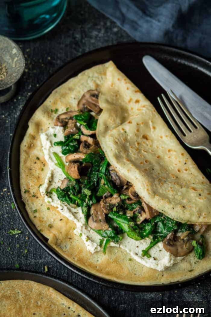 Vegan spinach and mushroom crepes with almond cheese - these savoury pancakes are a quick, easy, healthy and delicious plant based meal. #vegan #plantbased #veganmeal #vegancrepes #veganpancakes #eggless #dairyfree #vegancheese #vegandinner #veganbreakfast #veganbrunch #veganlunch #healthy #easy #pancakes #crepes #savourypancakes Close up of a vegan mushroom, spinach and cheese pancake on a black plate, showcasing the creamy filling.