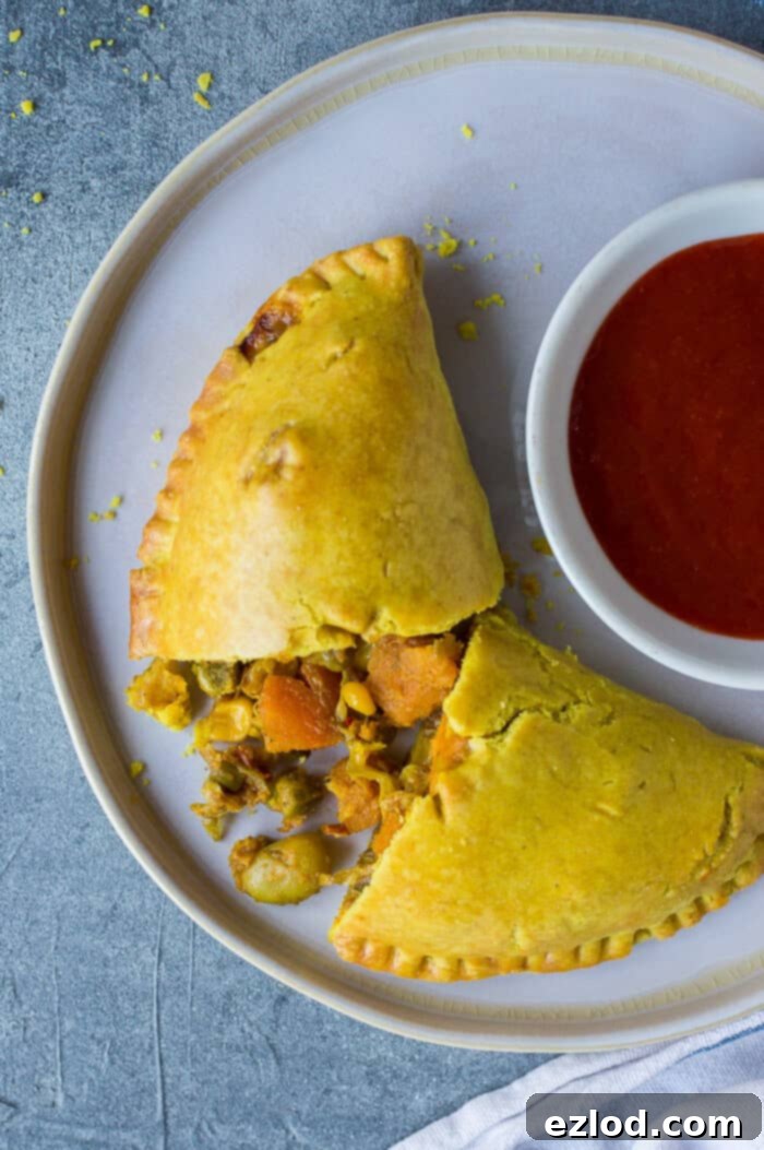 Irresistible Vegan Jamaican Veggie Patties 6 A perfectly baked vegan Jamaican vegetable patty on a white plate, accompanied by a small bowl of hot sauce, ready to be enjoyed.
