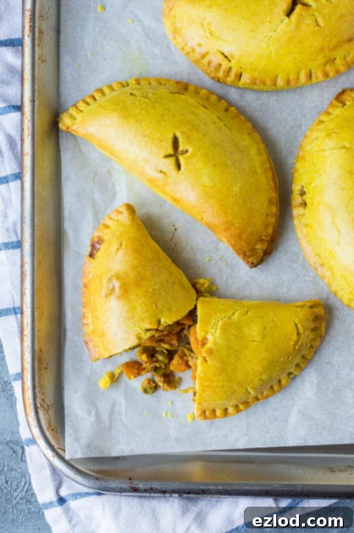 Irresistible Vegan Jamaican Veggie Patties 7 Close up of several golden, flaky vegan Jamaican vegetable pasties arranged on a silver baking tray, ready to be served or stored.